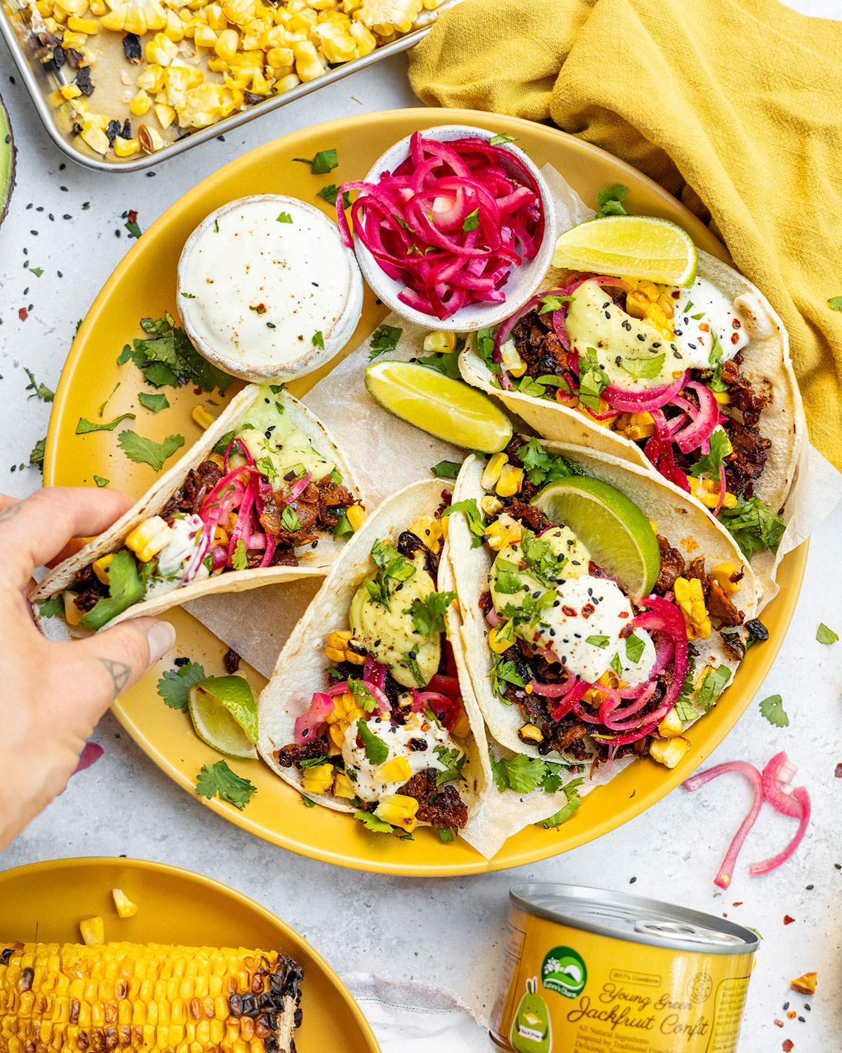 Jackfruit Carnitas tacos on a plate and a hand picking up one of the tacos.