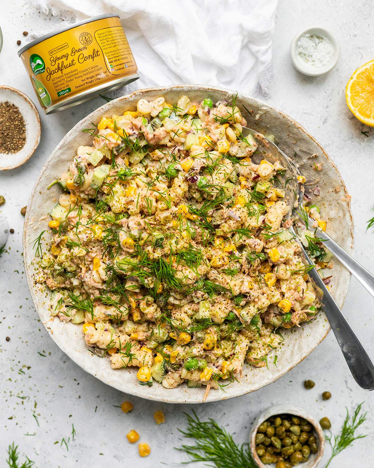Vegan Tuna pasta salad in a large serving bowl surrounded by ingredients, including a tin of jackfruit.