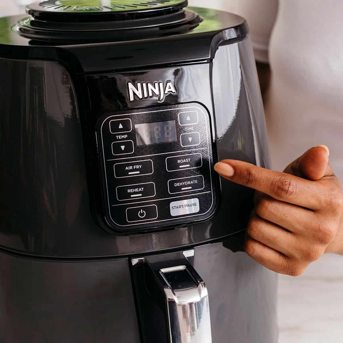 A hand pressing settings on an air fryer display.