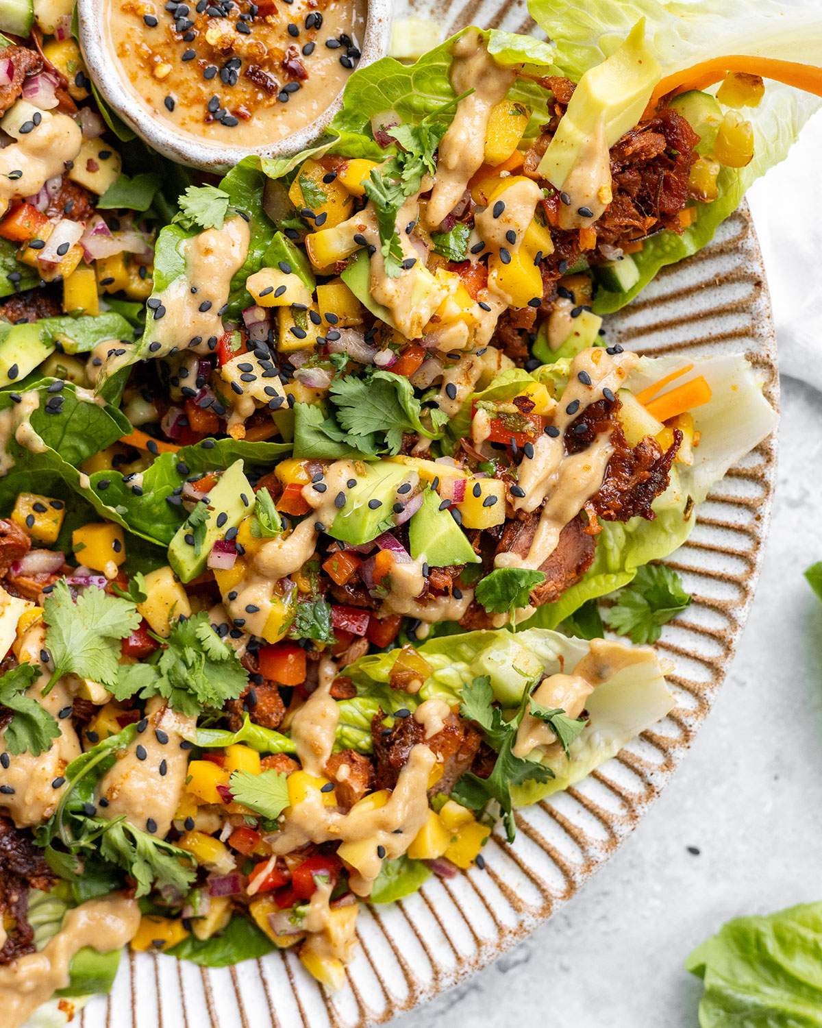 Spicy jackfruit lettuce wraps up close with a drizzly peanut sauce on the side.