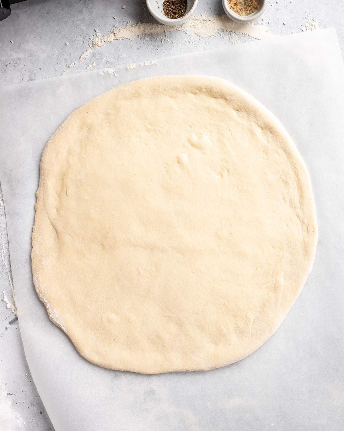 Round pizza dough on parchment paper.