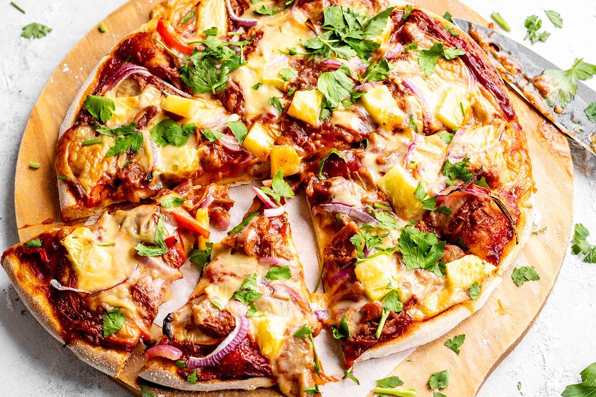 Homemade vegan BBQ pizza cut into slices on a serving board.