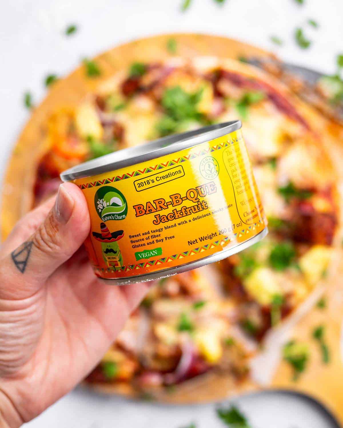 A hand holding a tin of BBQ jackfruit up close.