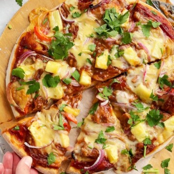 A hand picking up a slice of vegan bbq pizza.