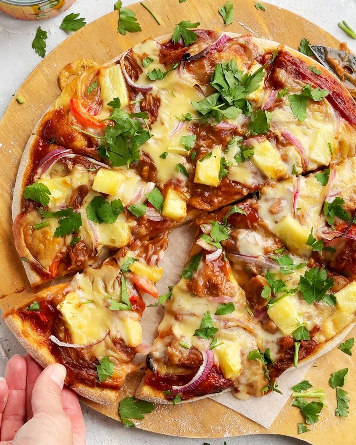 A hand picking up a slice of vegan bbq pizza.