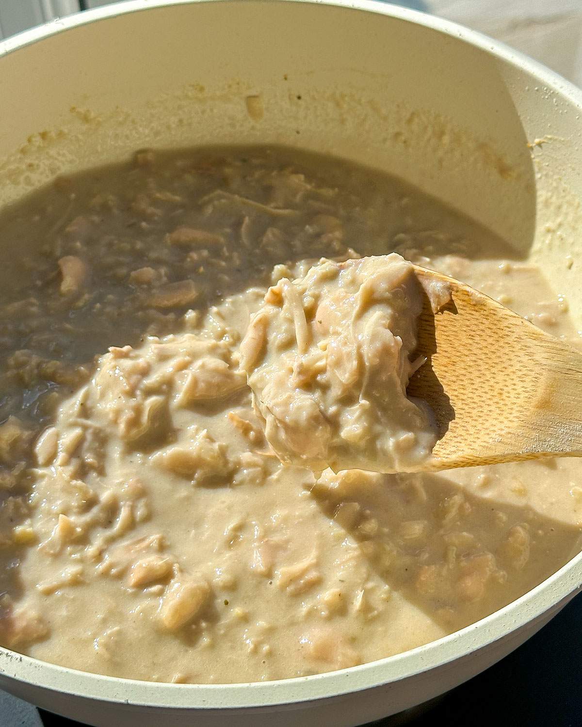 Stirring creamy jackfruit mix in a skillet with a wooden spoon.