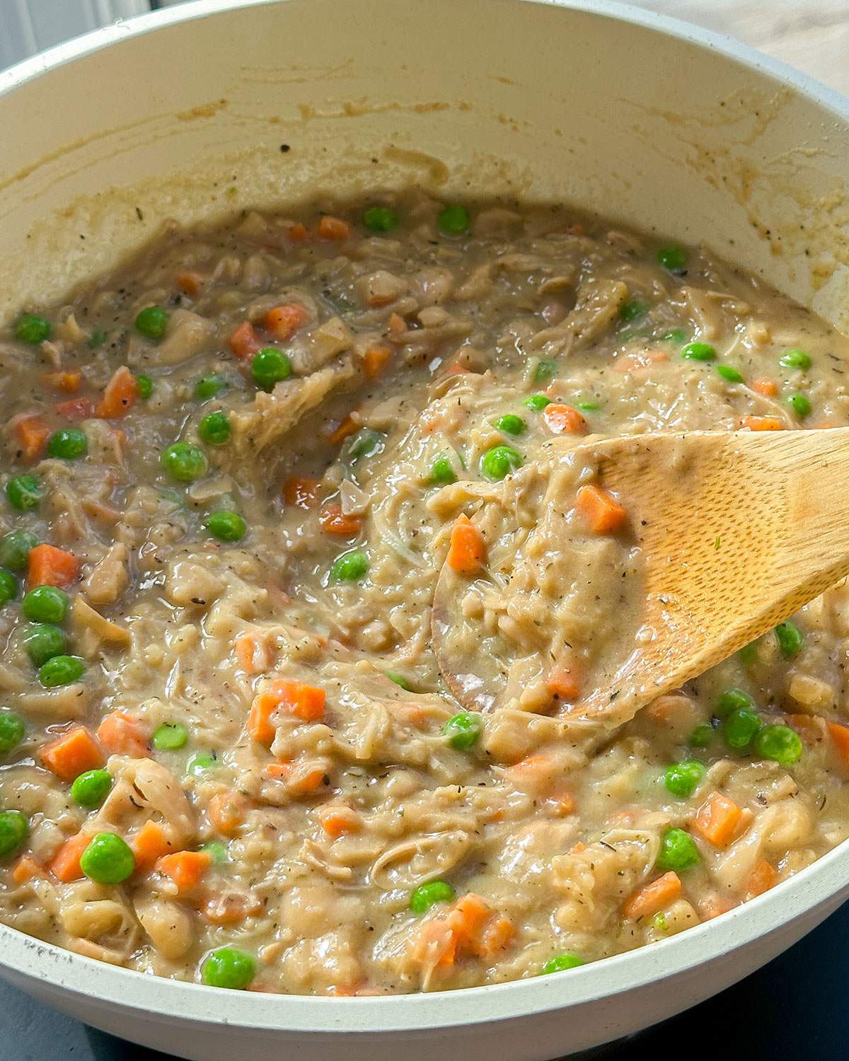 Stirring creamy vegan chicken pot pie filling in a skillet.