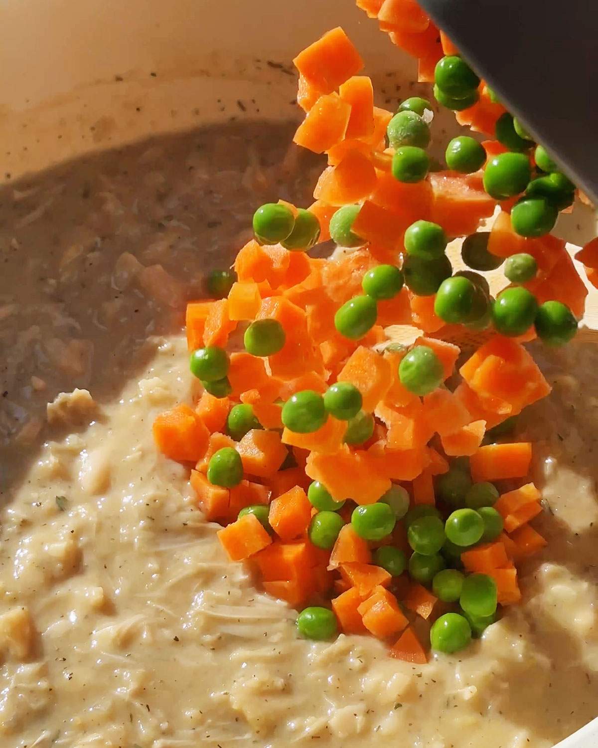 Adding peas and carrots to filling filling in skillet.