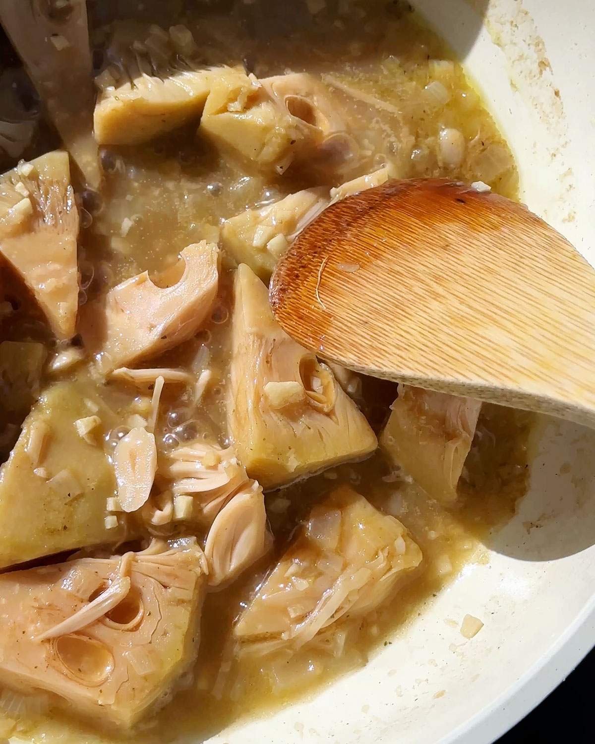Shredding jackfruit in a skillet with a wooden spoon.