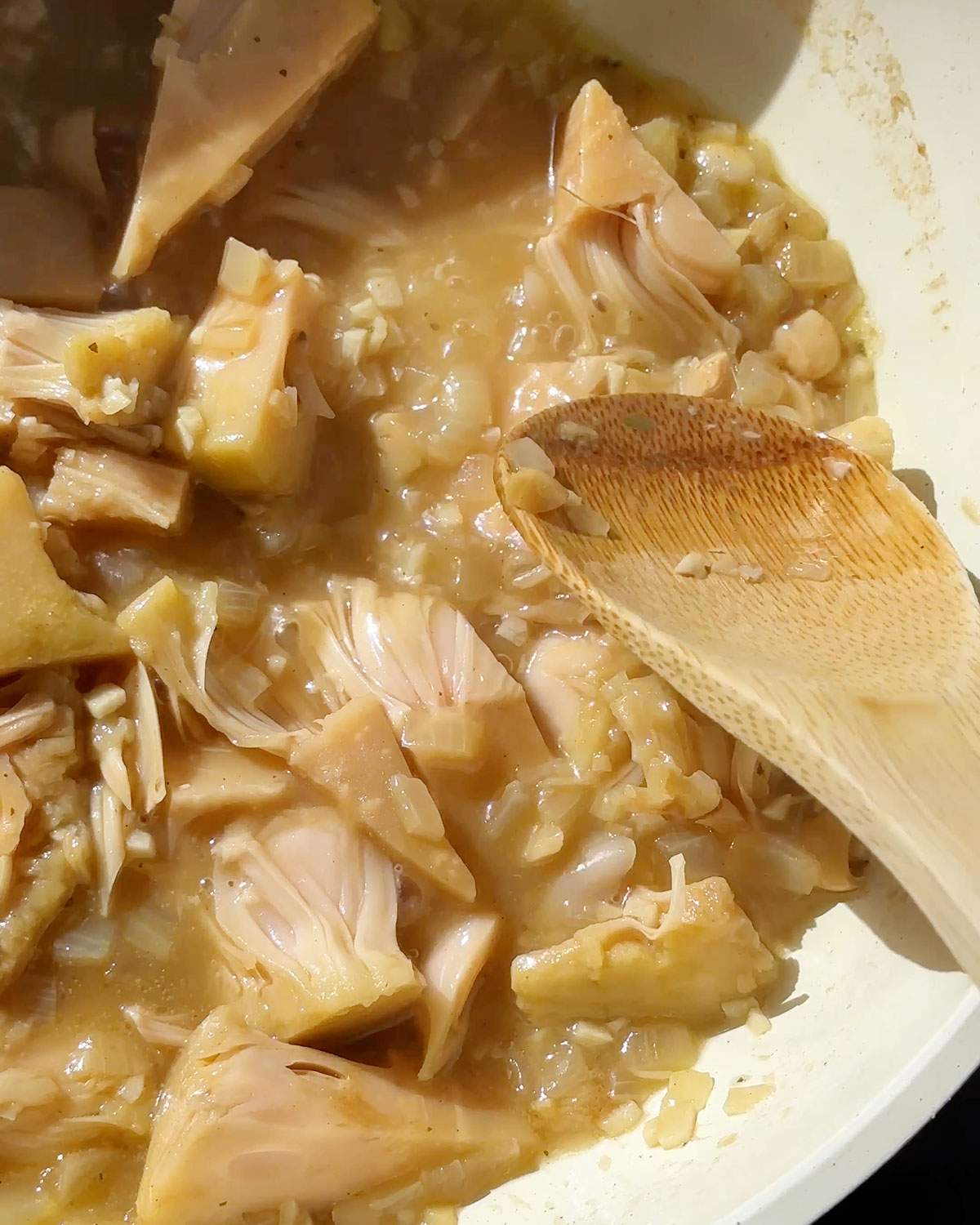 Shredding jackfruit in a skillet with a wooden spoon.
