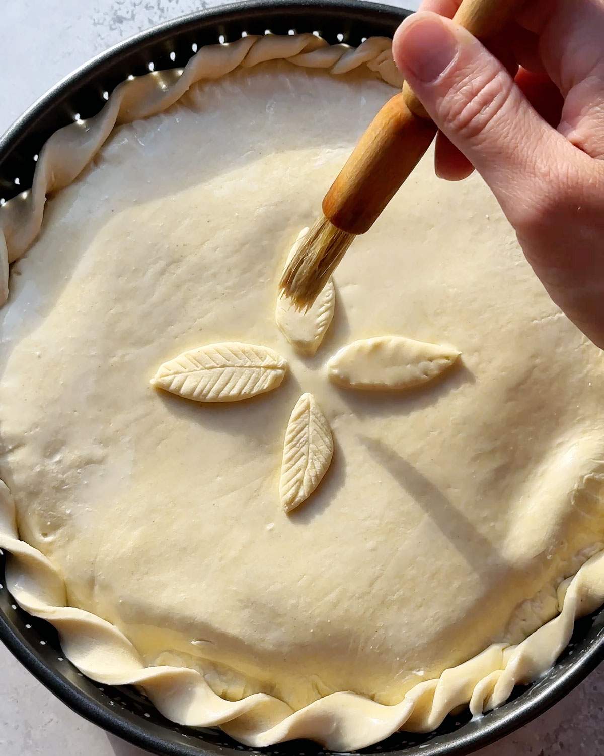 Brushing plant milk onto pot pie before baking.