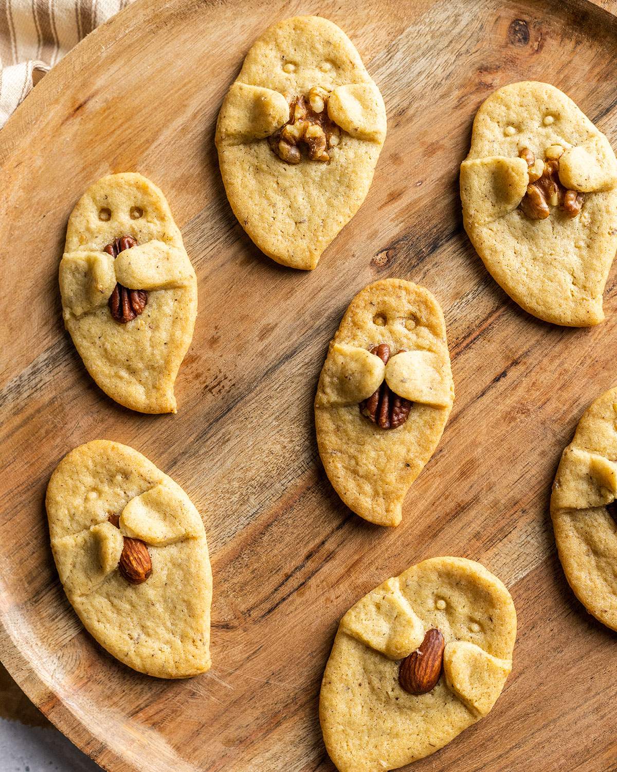 Cute ghost-shaped sugar cookies, each holding a nut, on a platter.