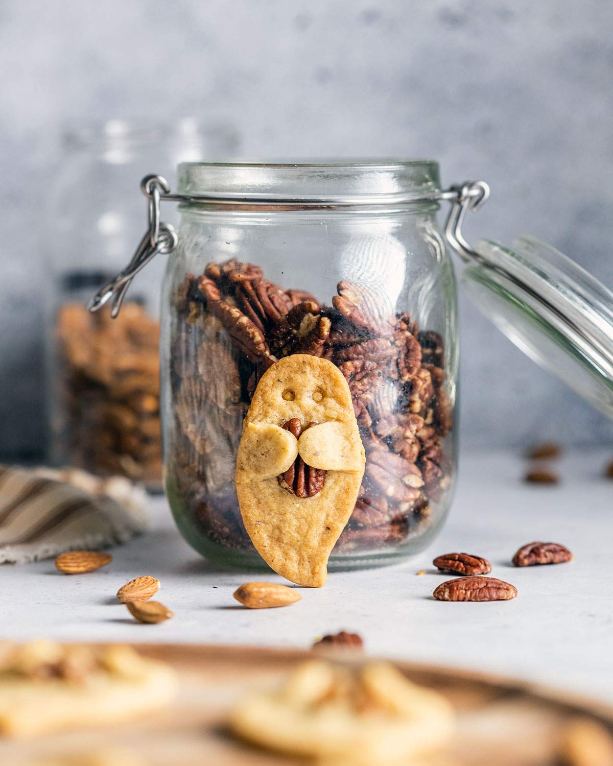 A ghost-shaped sugar cookie holding a pecan nut leaning against a jar of pecans.