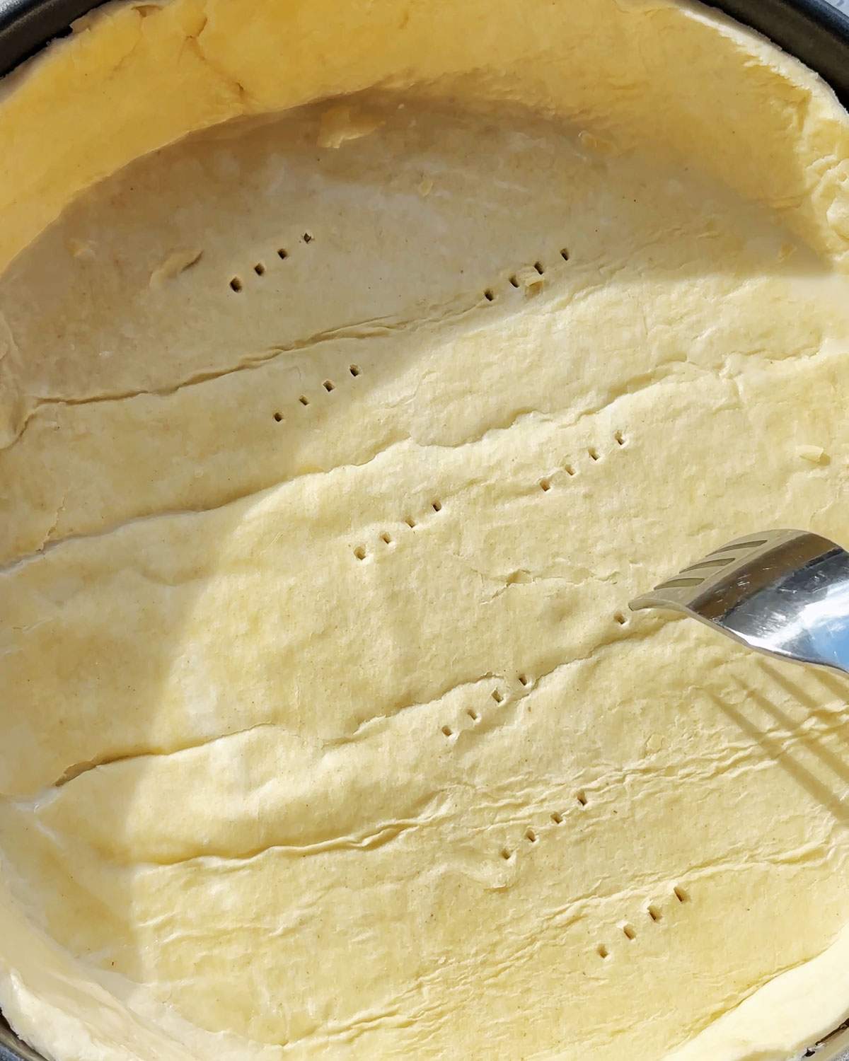 Piercing pie pastry bottom with a fork.