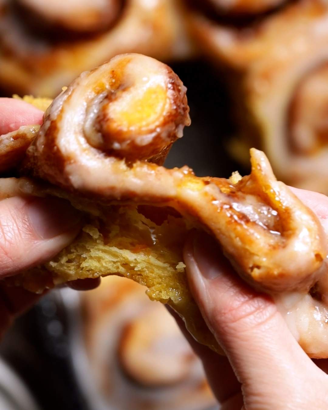 Hands ripping a soft, fluffy cinnamon roll.