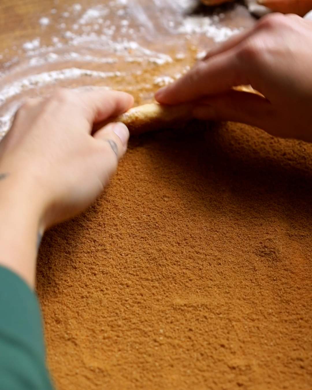 Hands rolling up cinnamon roll dough.