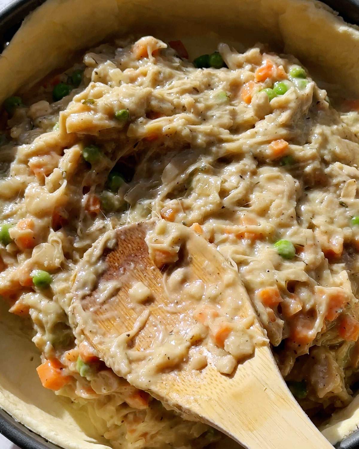 Spreading pie filling in pie crust with a wooden spoon.