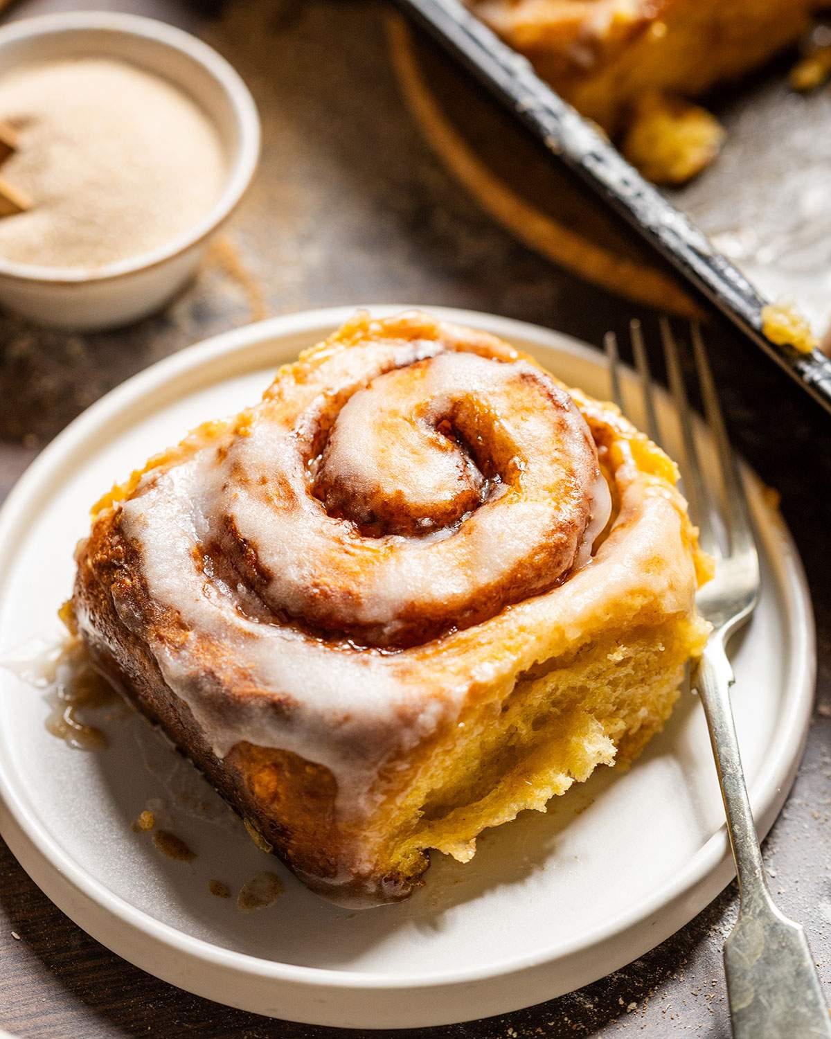 A fluffy sweet potato cinnamon rolls with glaze on a small plate with a fork.