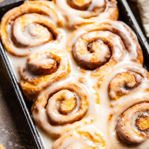 Fluffy Vegan Sweet Potato Cinnamon Rolls in a baking dish with glaze on top.