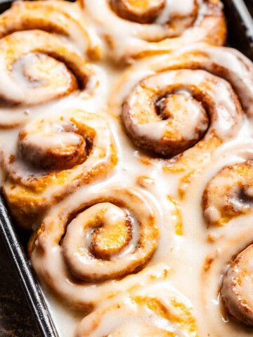 Fluffy Vegan Sweet Potato Cinnamon Rolls in a baking dish with glaze on top.