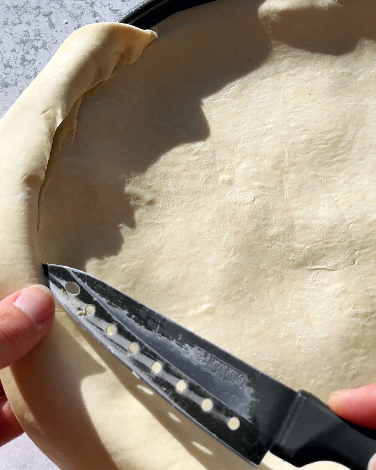 Trimming excess pastry from puff pastry sheet.
