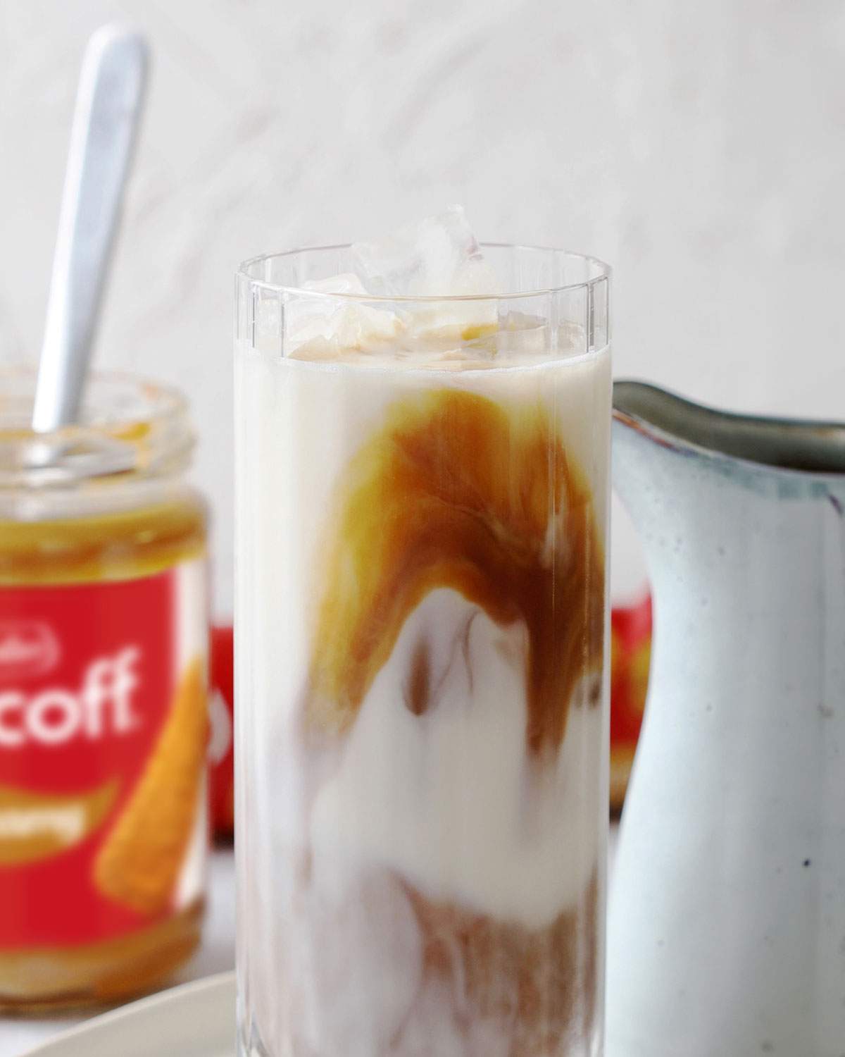 A tall glass with iced biscoff latte with swirls of melted biscoff clearly visible.