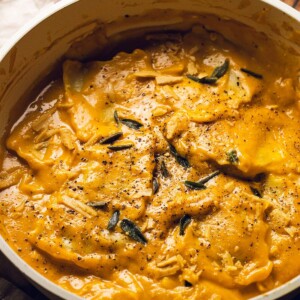 A skillet with ravioli in a creamy pumpkin sauce and sage on top.
