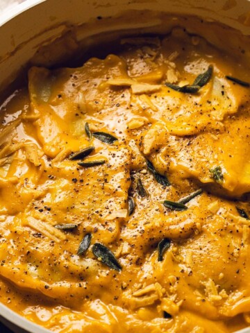 A skillet with ravioli in a creamy pumpkin sauce and sage on top.
