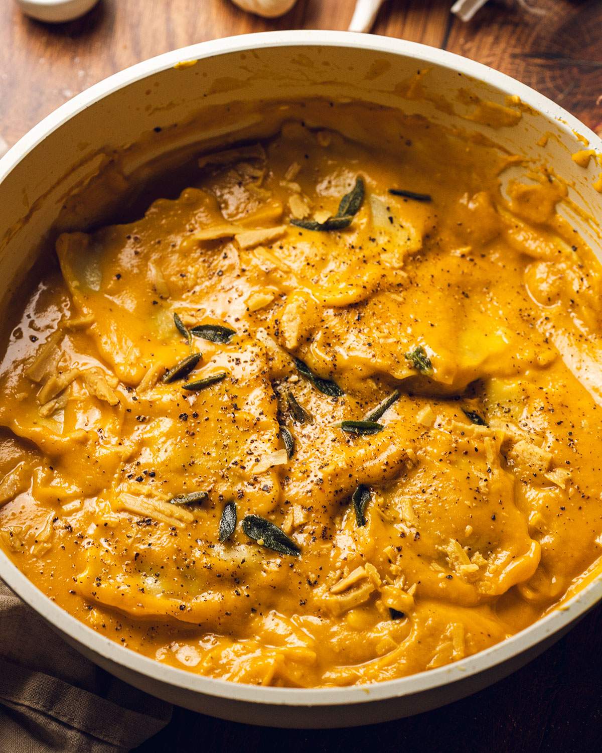A skillet with ravioli in a creamy pumpkin sauce and sage on top.