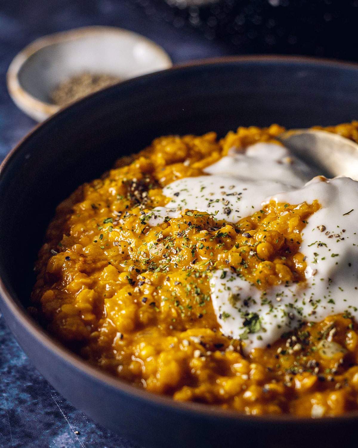 Pumpkin Dhal in a dark bowl with coconut yogurt on top.