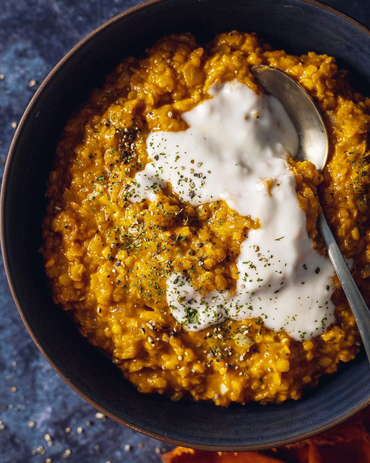 Roasted pumpkin curry dhal in a black bowl with yogurt and fresh herbs on top.