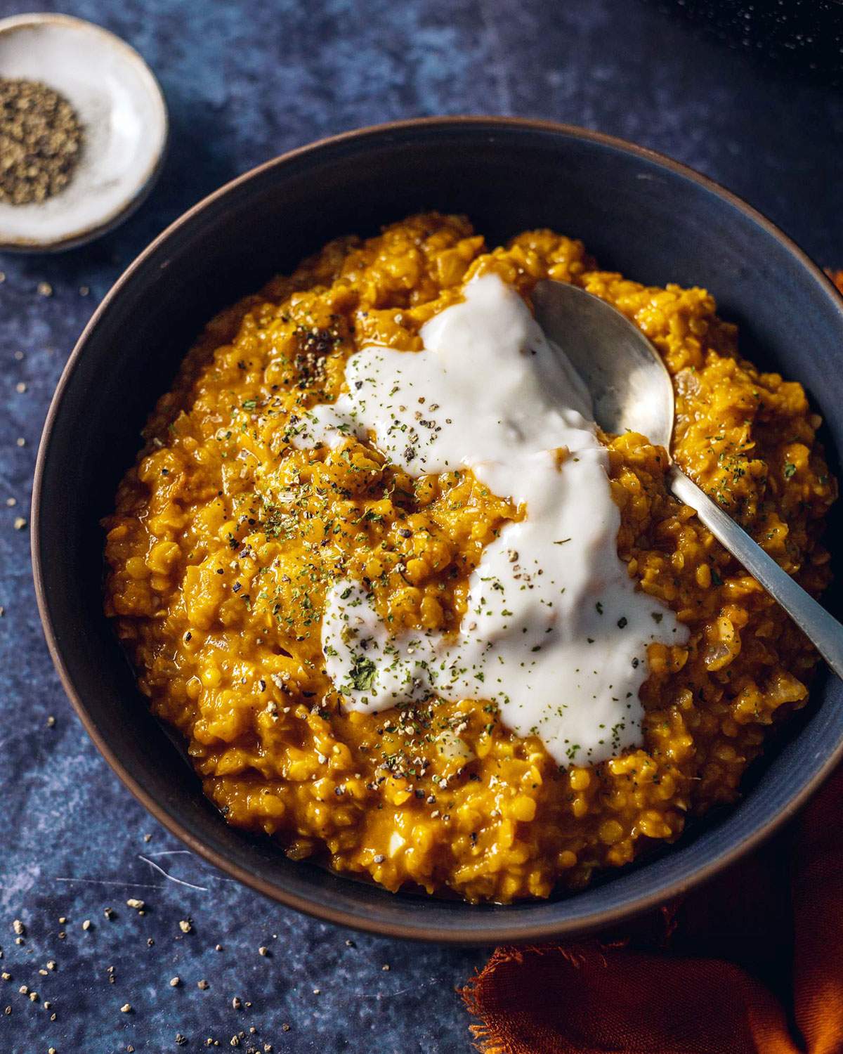 A bowl filled with red lentil dhal with a spoon on the side and coconut yogurt on top.
