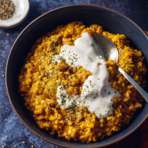 A bowl filled with red lentil dhal with a spoon on the side and coconut yogurt on top.