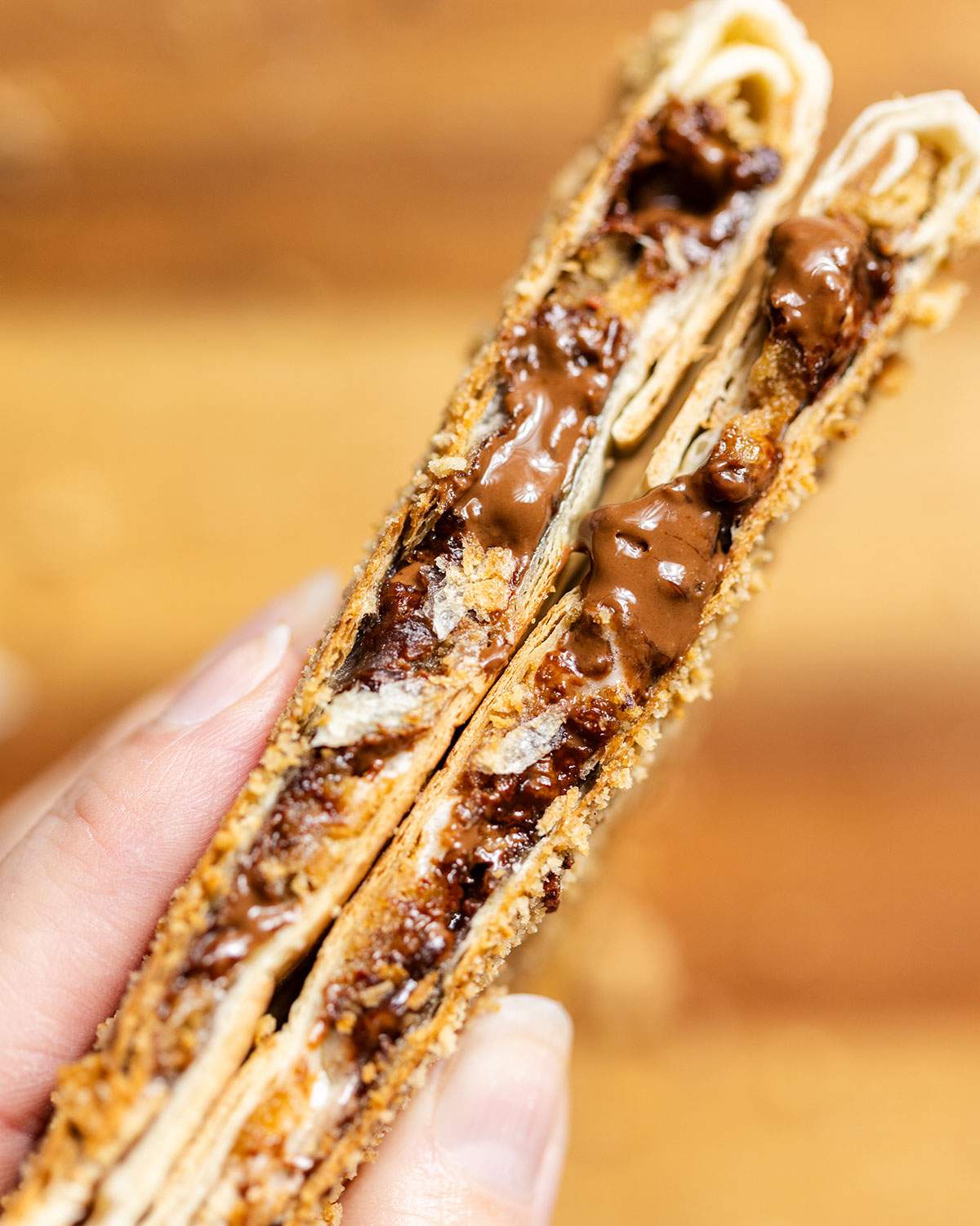 A hand holding two halves of smores crunchwrap with chocolate and marshmallow inside.