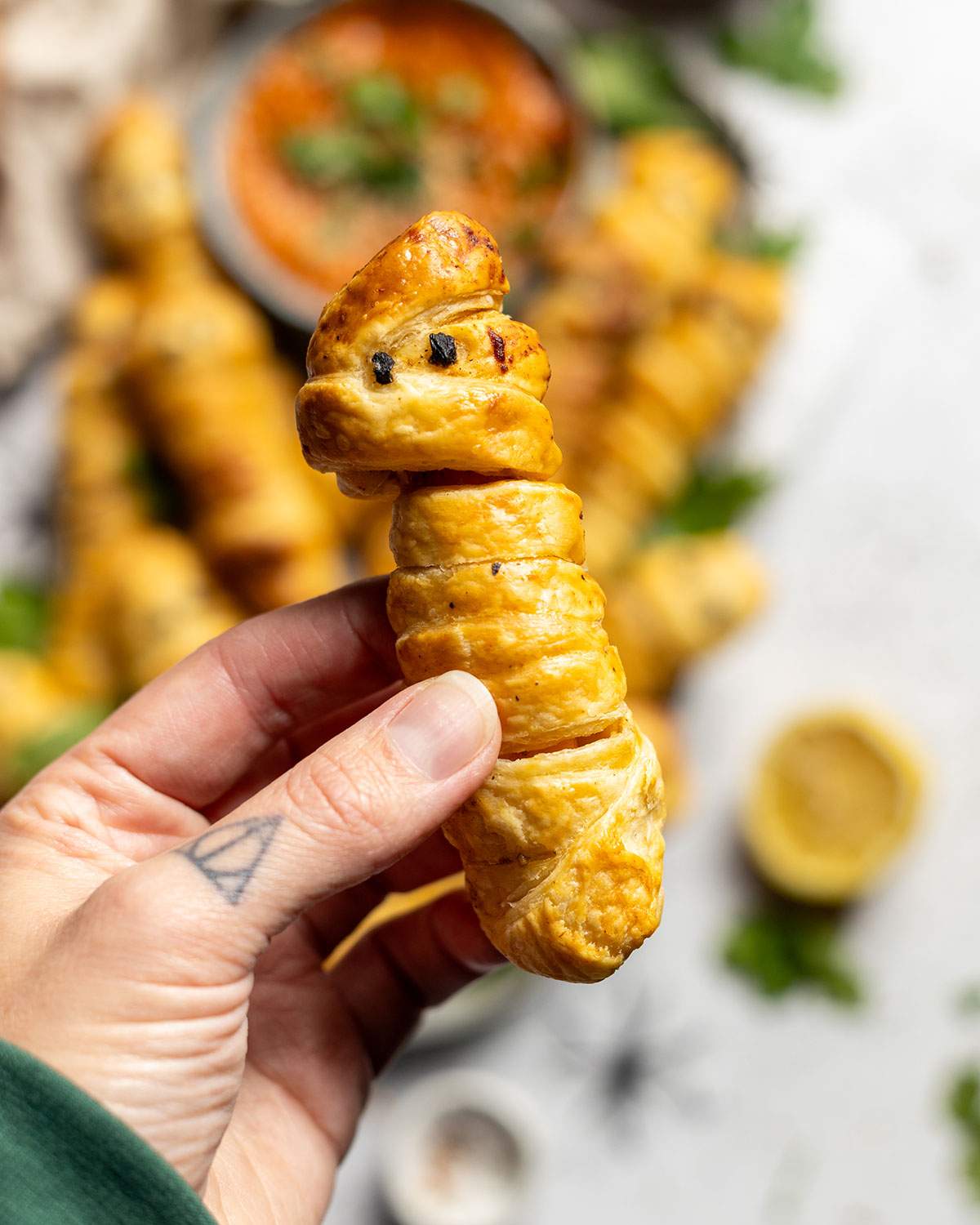 A hand holding a pastry wrapped sweet potato mummie.