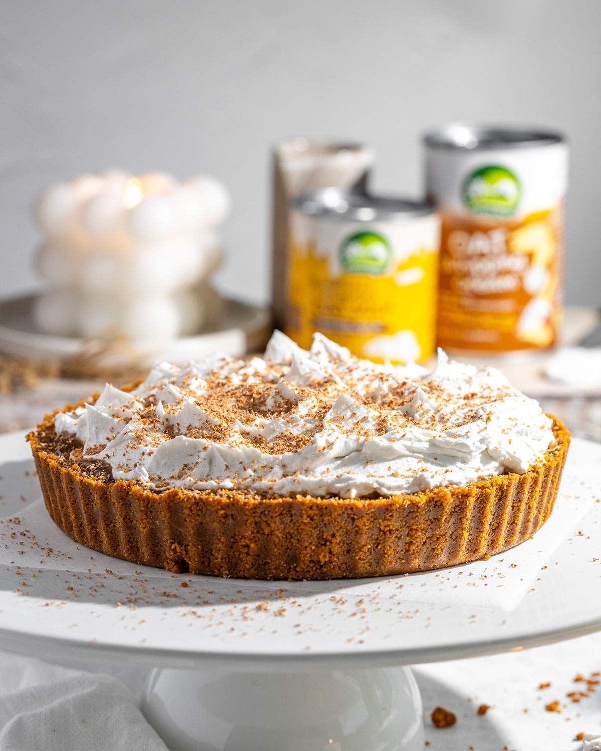 Vegan banoffee pie topped with whipped oat cream on a white cake stand ready to serve.