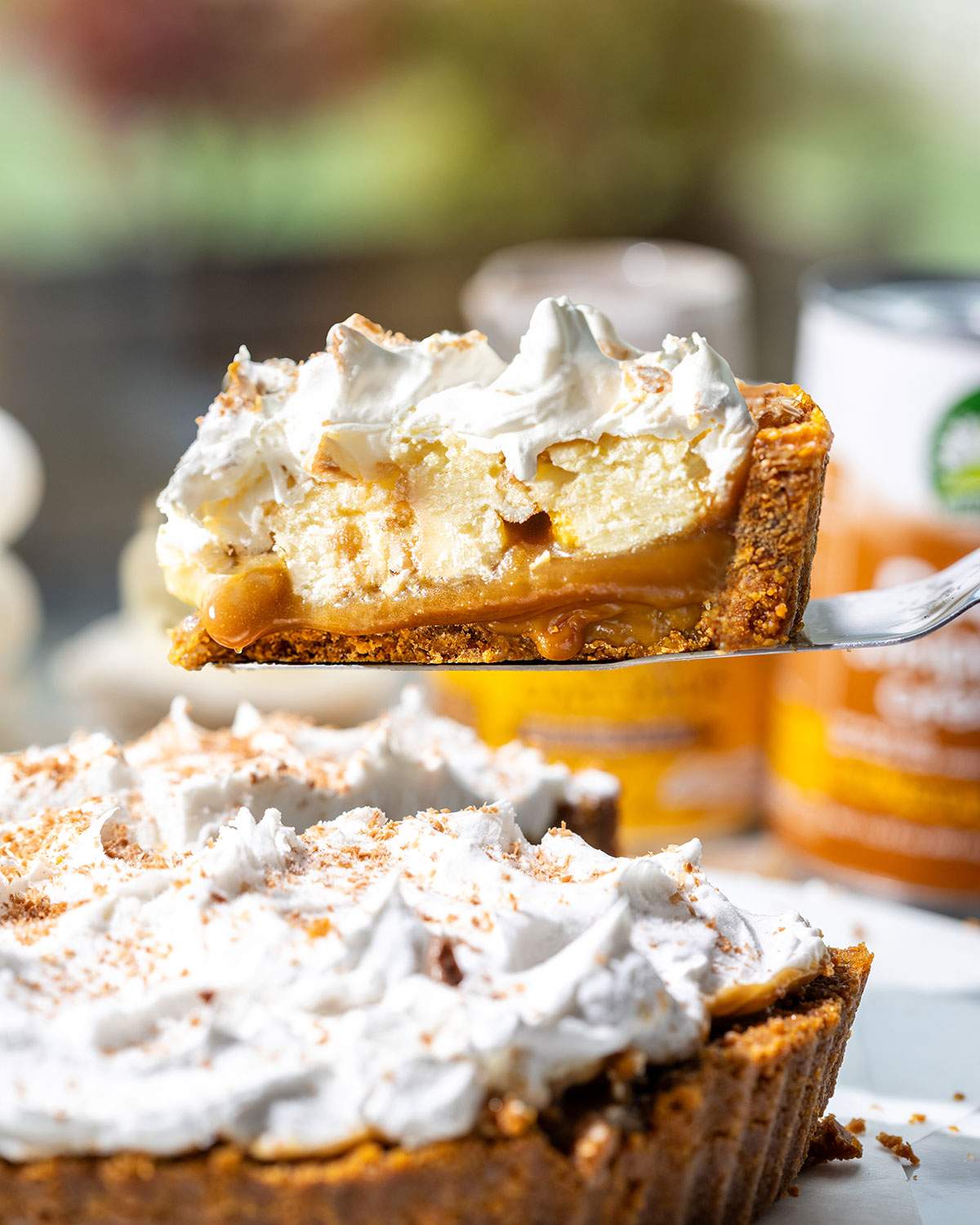 A slice of vegan banoffee pie lifted from the pie with layers of biscuit base, toffee sauce, banana slices and whipped vegan cream visible.