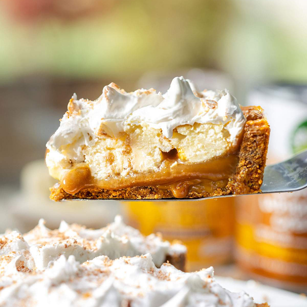 A slice of vegan banoffee pie lifted from the pie with layers of biscuit base, toffee sauce, banana slices and whipped vegan cream visible.