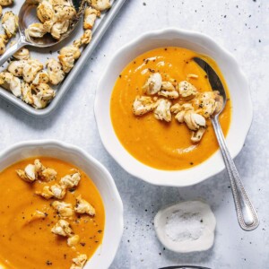 Two bowls with roasted butternut squash soup on a white table.