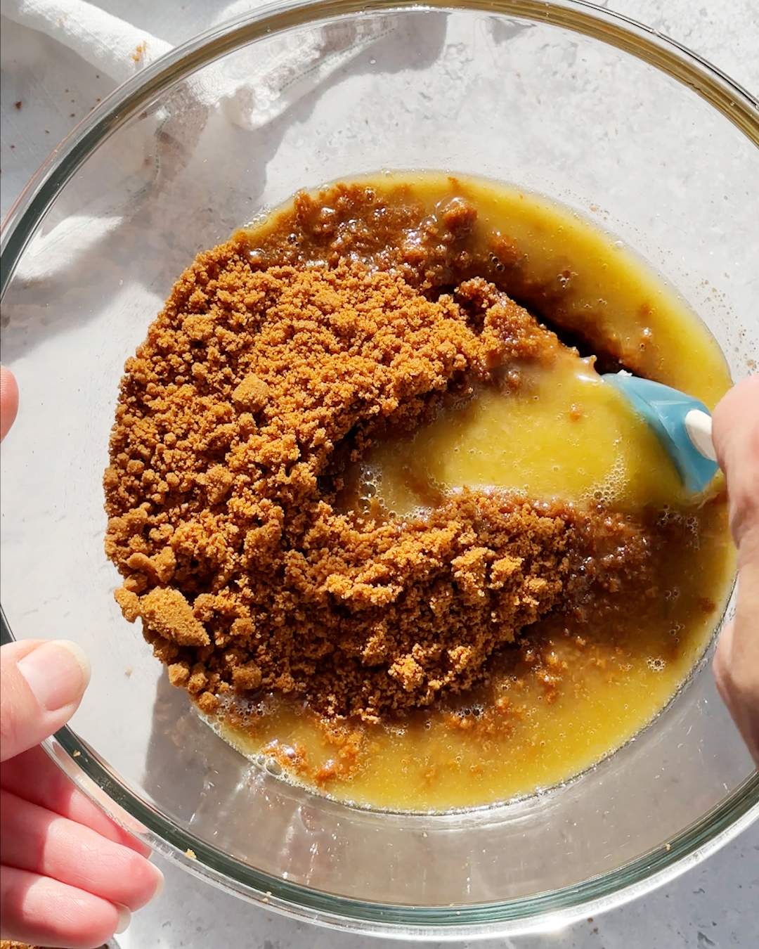 Mixing crushed biscuits and melted butter in a bowl.