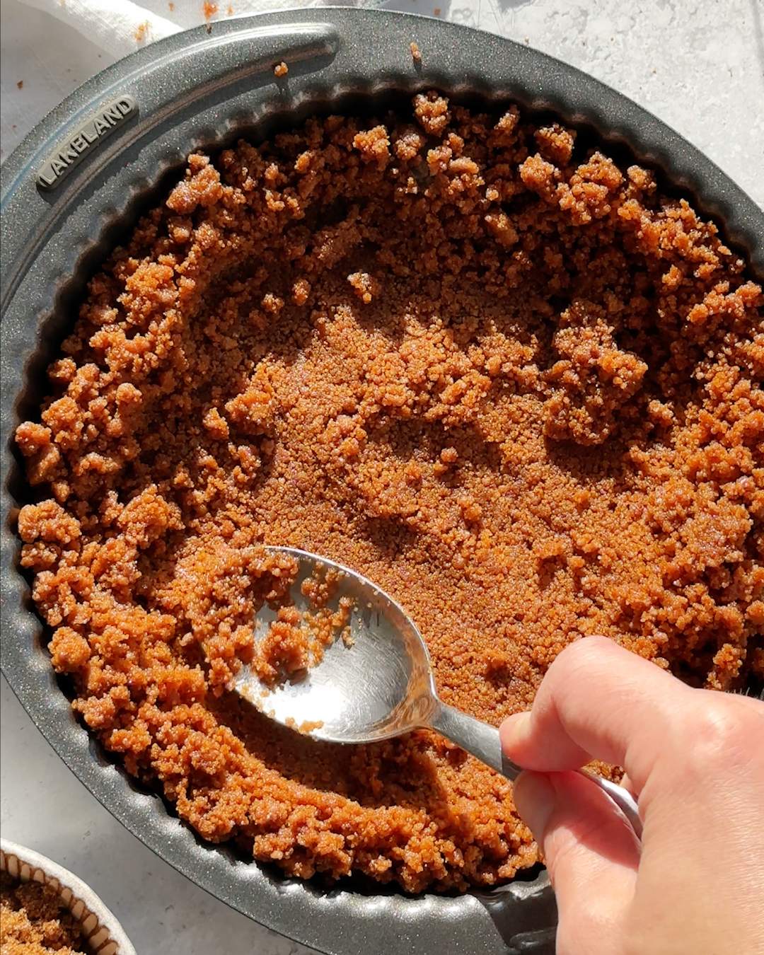 Pressing biscuit base into pie dish with a spoon.