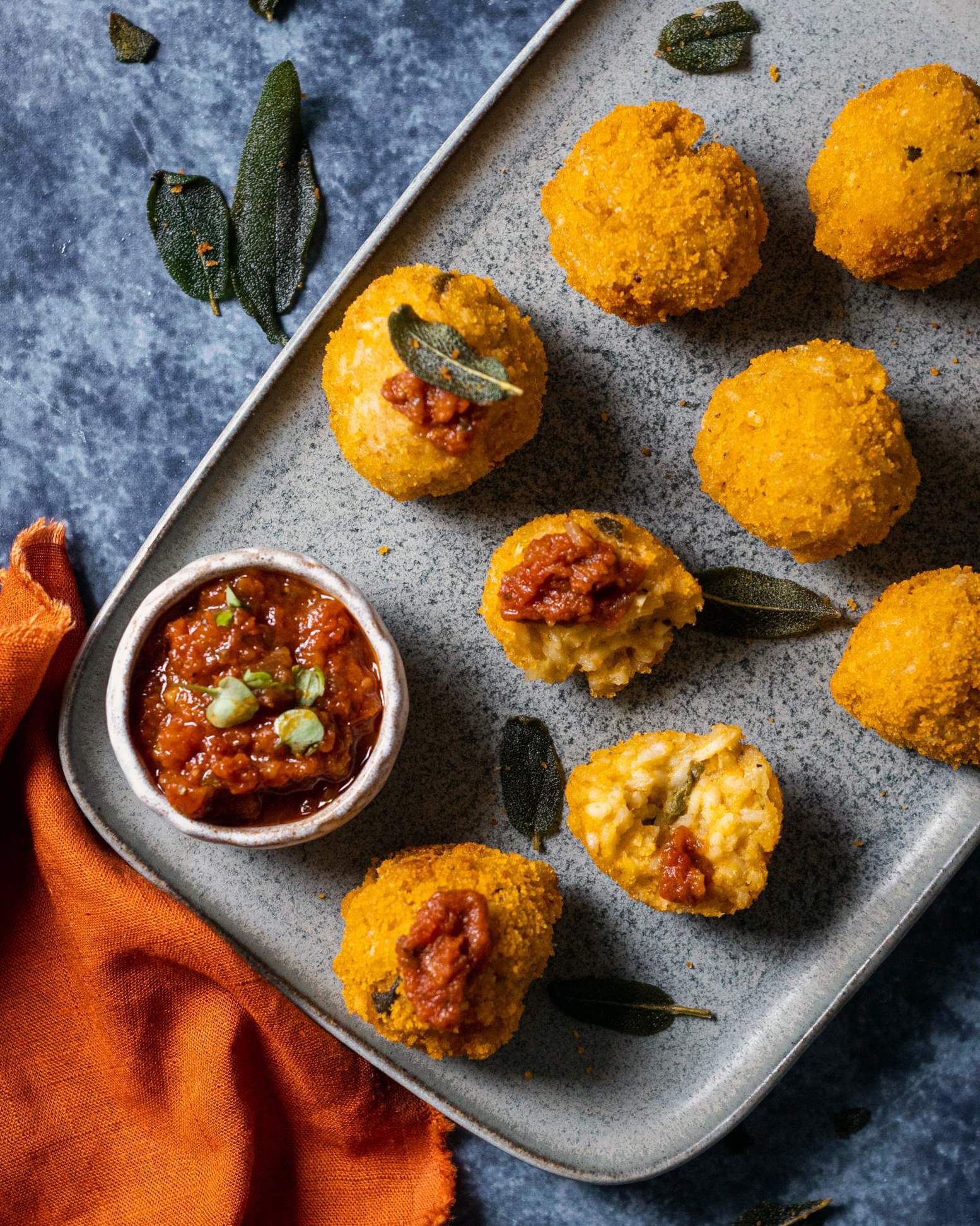 Pumpkin arancini balls on a serving platter alongside a dip and crispy sage leaves.