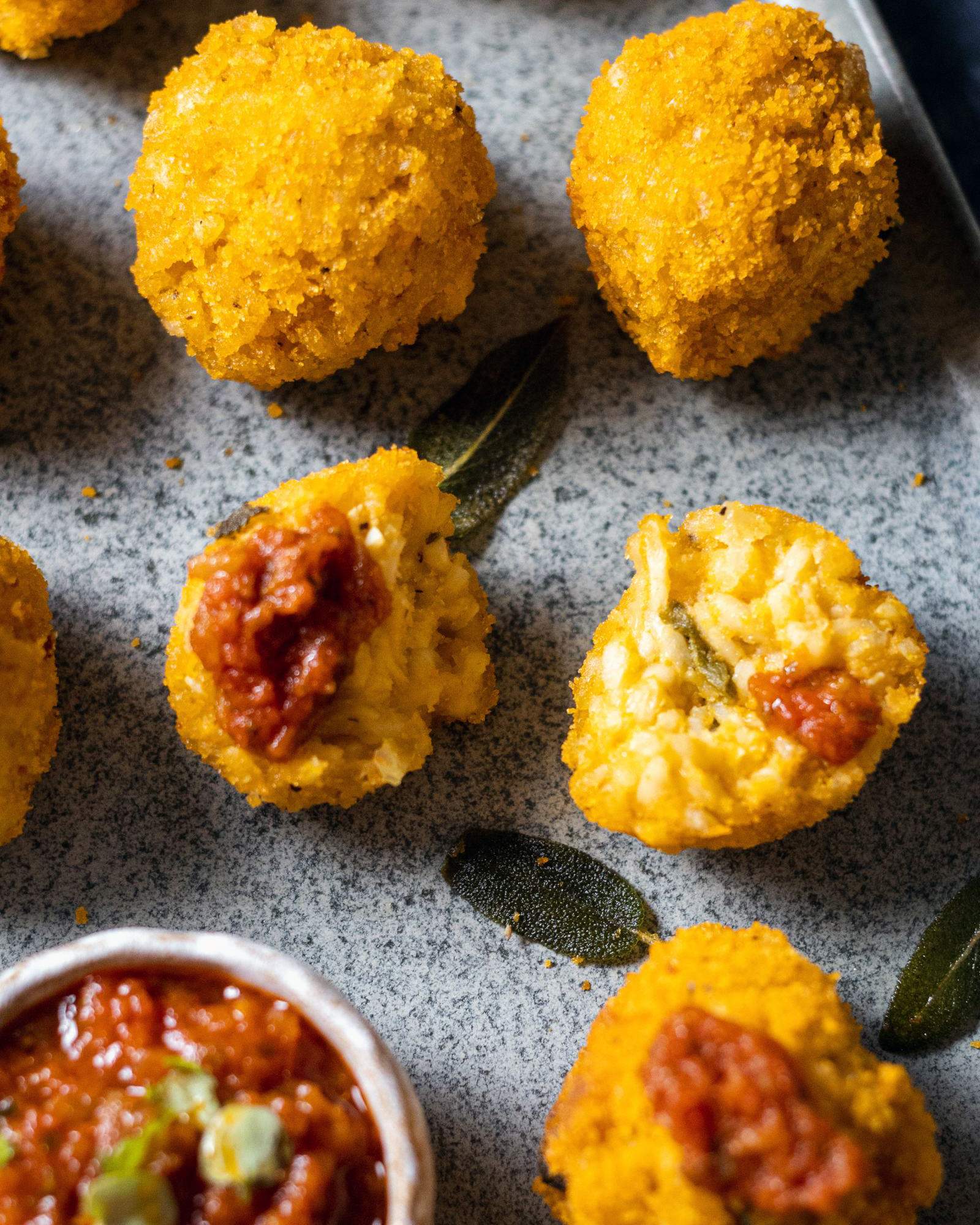 Pumpkin arancini on a platter with one arancini cut in half, showing the creamy pumpkin risotto inside.