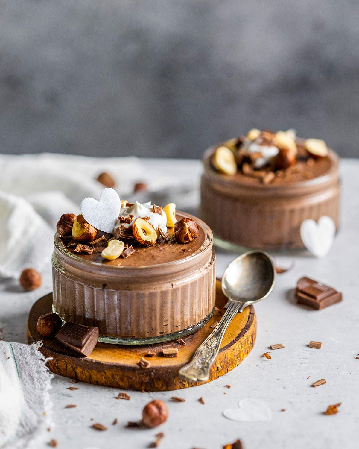 Two jars with vegan chocolate mousse with hazelnuts on top on a table.