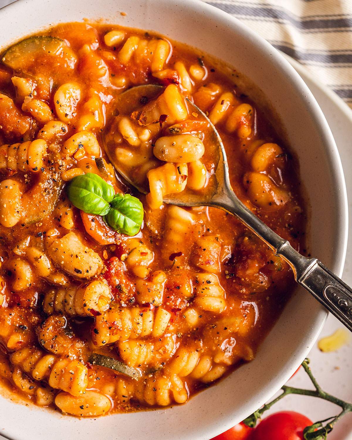 A spoon in a bowl of plant based minestrone soup with mixed pasta.