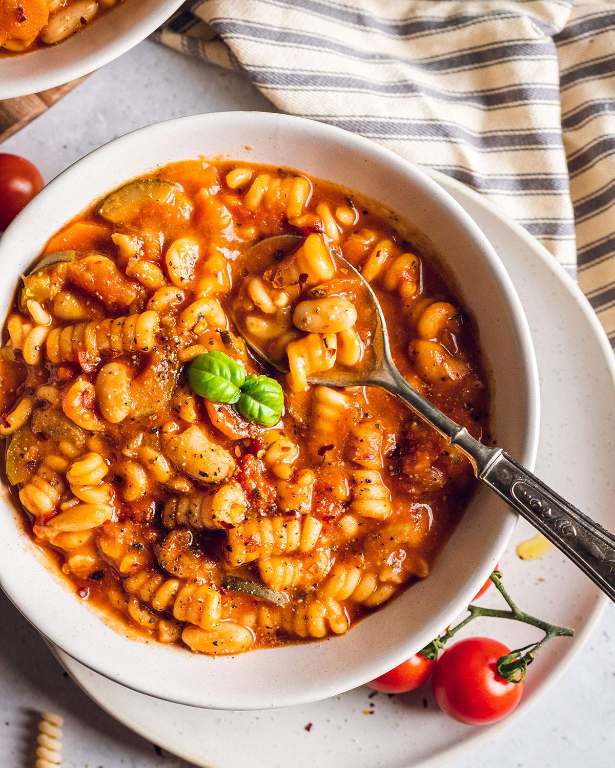 A spoon in a bowl of minestrone soup with mixed pasta.