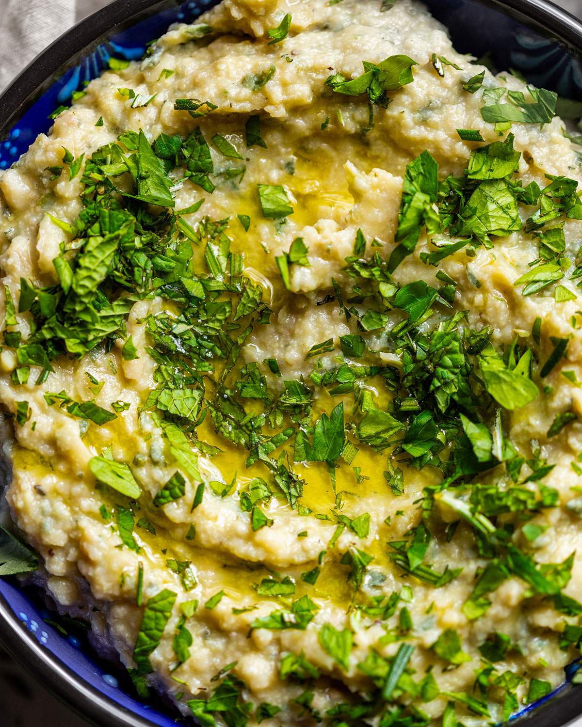 Herb butter bean mash up close with a drizzle of oil and herbs on top.