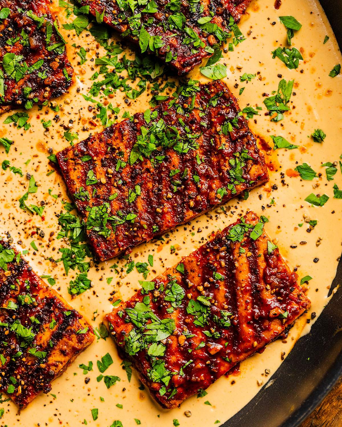 Cajun tofu steaks in a skillet with cajun alfredo sauce.