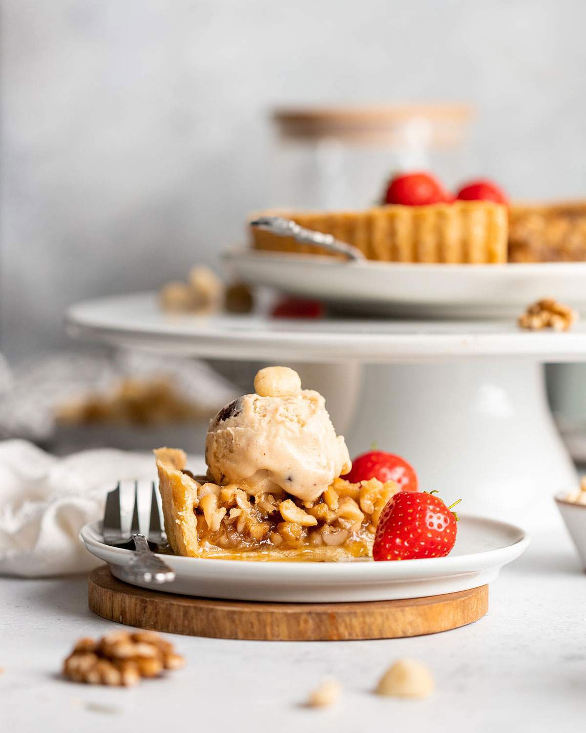 A slice of vegan caramel tart on a plate with fresh strawberries and ice cream.