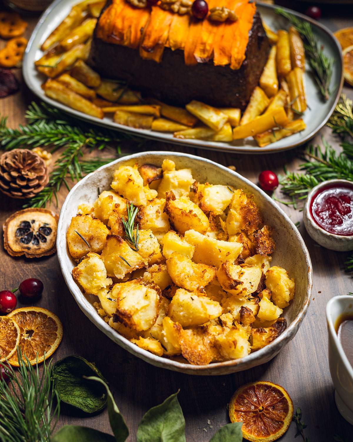 Vegan roast potatoes in an oven dish on the dinner table next to a nut roast.